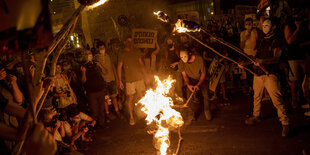 Eine Menschenmenge steht um ein Feuer herum. Einige halten Plakate in den Händen.