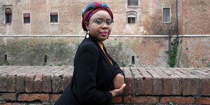 Die Schriftstellerin Ayobami Adebayo lehnt an einem gemauerten Geländer.