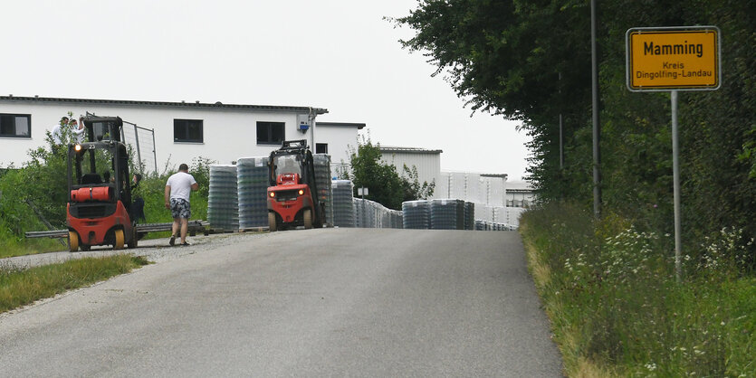 Eine Landstraße und ein gelbes Schild mit der Aufschrift "Mamming", im Hintergrund ein weißes Gebäude