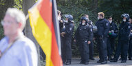 Ein alter Mann mit Deutschland-Fahne läuft auf der Demonstration in Berlin am Samstag an Polizist*innen vorbei