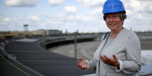 Die Bausenatorin steht mit einem Bauhelm auf einer Baustelle