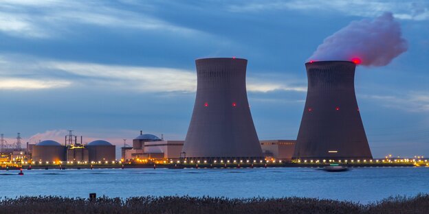 Zwei Reaktoren des Kernkraftwerks Doel vor einem See in der Abendsonne.