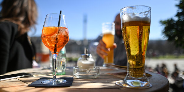 Ein Glas mit Aperol Spritz und ein Bierglas in einem Biergarten im Sommer