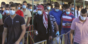 Masse an Männern mit Mundschutzmasken an einem Checkpoint