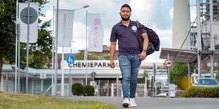 Mann in Jeans und dunklem Shirt läuft vor einem Industriegelände