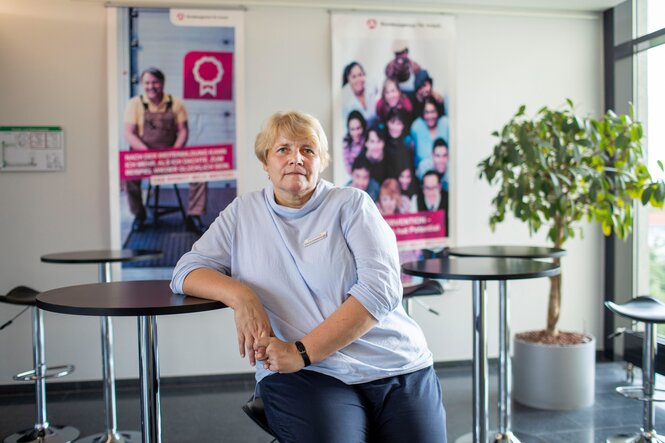 Eine Frau im grauen Pullover vor Plakaten der Agentur für Arbeit