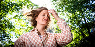 Sängerin Wilhelmine steht in einem Garten voller Bäume und ist mit viel Licht von oben fotografiert und fasst sich ins Haar dabei