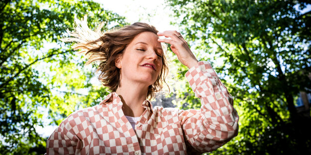 Sängerin Wilhelmine steht in einem Garten voller Bäume und ist mit viel Licht von oben fotografiert und fasst sich ins Haar dabei