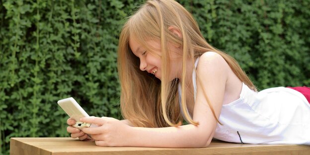 ein Mädchen liegt im Freien auf einer Liege und spielt mit ihrem Handy
