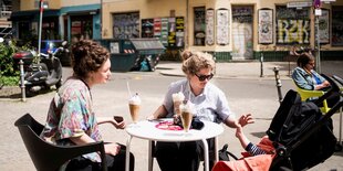 Zwei Frauen mit Kinderwagen am Bistrotisch, darauf große Becher mit Eiskaffee