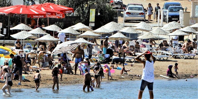 Viele Menschen halten sich dichtgedrängt unter Sonnenschirmen am Strand auf