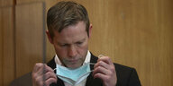 Stephan Ernst nimmt vor Gericht eine OP-Maske ab, die er zum Schutz vor dem Coronavirus getragen hat