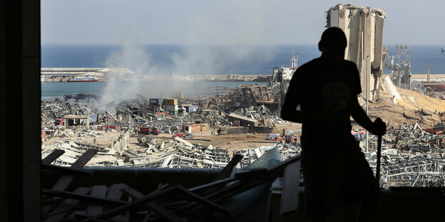 Schattenriss eines Mannes, der aus einer zerstörten Wohnung auf den zerstörten Hafen schaut