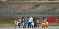Eine Gruppe von Menschen mit Masken läuft über das Flugfeld eines Flughafens