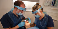 Ein Zahnsrzt und eine Assistentin behandln einen Patienten und tragen dabei Sicherheitsausrüstung wegen CoronaT