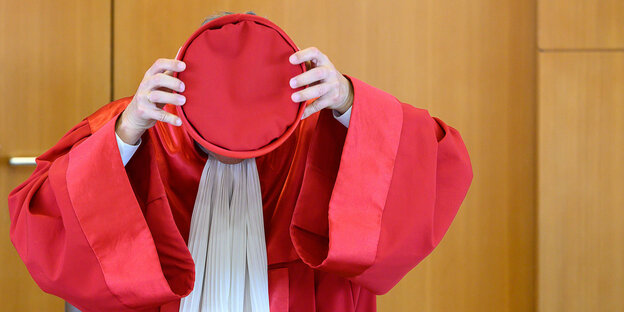 Bundesverfassungsrichter hält sich einen roten Hut vors Gesicht