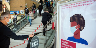 Mann mit Maske auf einer Rolltreppe