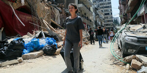eine Anwohnerin zieht ihren Koffer durch eine von Ruinen gesäumte Strasse