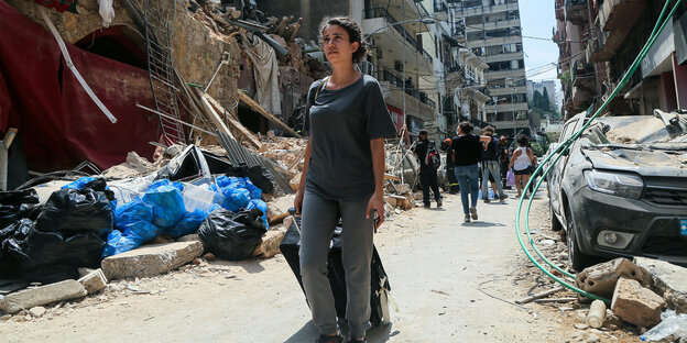 eine Anwohnerin zieht ihren Koffer durch eine von Ruinen gesäumte Strasse