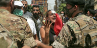 Eine Frau spricht aufgergt mit Soldaten, sie trägt einen Verband am Kopf
