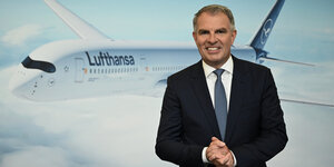 Portrait von Carsten Spohr vor einem Foto mit Lufthansaflugzeug