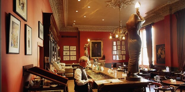 ein Mann an der Bar des Shelbourne Hotel wo auf dem Tresen zwei Statuen stehen
