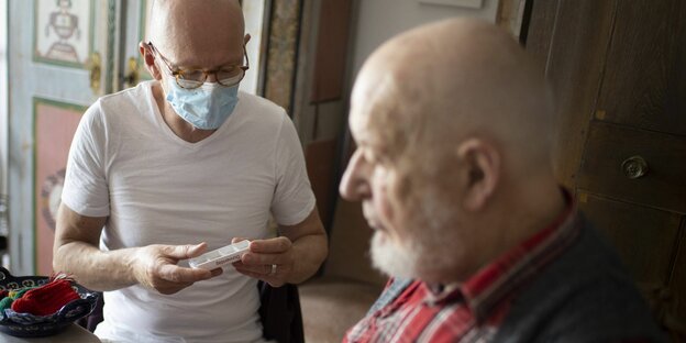 tenpfleger kontrolliert die Medikamenten Einnahme eines alten Mannes