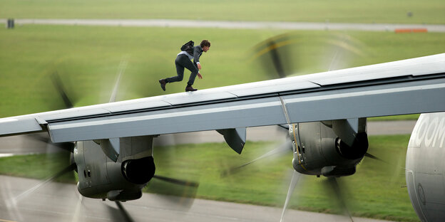 Hollywood-Schauspieler Tom Cruise (als Ethan Hunt) läuft auf der Tragfläche eines Militärjets - eine Szene aus "Mission: Impossible Rogue Nation"