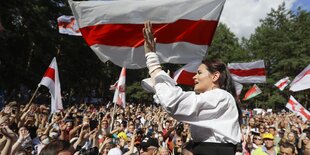 Swetlana Tichanowskaja bei einer Veranstaltung. Sie ragt über die Köpfe von vielen Protestierenden hinaus und ruft etwas. Die Frau hat lange Haare. Überall sind Fahnen von Belarus.