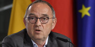 SPD-Chef Norbert Walter-Borjans vor den Fahnen von Deutschland und der EU. Er ist ein alter Mann mit rundem Kopf und Doppelkinn. Er trägt eine runde Brille und hat lichtes, kurzes Haar.