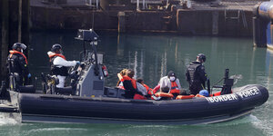 Ein Schlauchboot der britischen Grenzpolizei. In dem Boot befinden sich Polizisten und Geflüchtete. Die Polizisten tragen Schwimmwesten und Helme mit Visier. Die Geflüchteten nur Schwimmwesten.