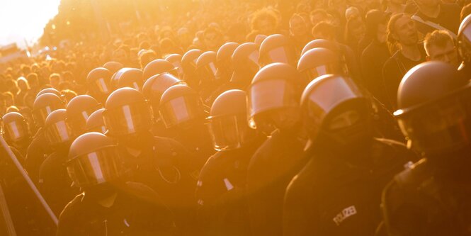 Behelmte Polizisten neben einer Demo im Gegenlicht der untergehenden Sonne