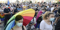 Demonstrantinnen für LGBT-Rechte in Warschau. Sie tragen Masken und eine Frau hat einen Regenbogenregenschirm über sich gespannt.