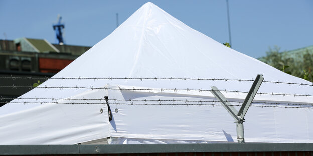 Zelt-Dach vor einer Mauer mit Stacheldraht
