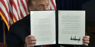 US-Präsident Trump hält eine Kladde mit unterschriebenen Dokumenten hoch