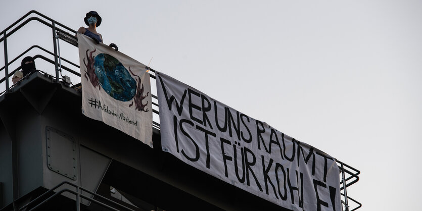 Vermummte Aktivist*innen auf einem mit Bannern geschmückten Turm des Kraftwerks