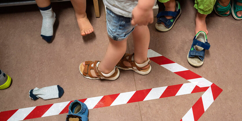 ein Kinderfüsse, Pfeil ist mit rot/weißem Klebeband auf den Boden geklebt