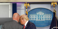 Ein Mann flüstert Trump im Presse-Saal des Weißen Hauses etwas ins Ohr.