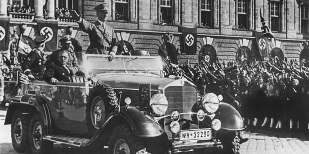 Adolf Hitler grüßt aus einem Auto beim Einmarsch in Wien
