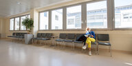 Eine Frau mit Mundschutz sitzt als einzige in einer leeren Stuhlreihe, im Wartezimer eines Krankenhauses