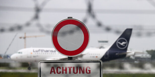 Flugzeug der Lufthansa hinter Verkehrsschild und Zaun.