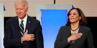 Joe Biden und Kamala Harris stehen nebeneinander und haben die Hand auf dem Herzen.