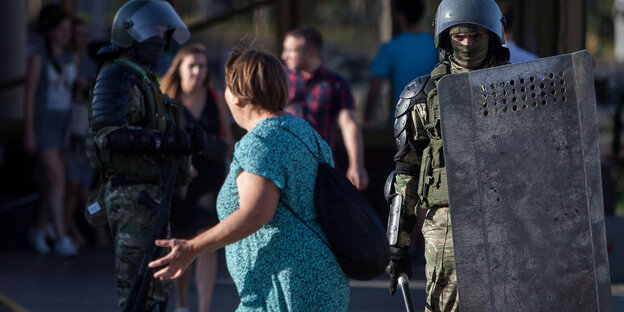 Eine Frau in grünem Kleid steht bewaffneten Sicherheitskräften gegenüber.