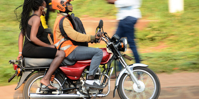 Auf einem Motorrad sitzt ein Mann mit Helm, auf dem Rücksitz eine Frau ohne Helm.