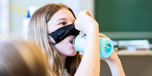 Ein Mädchen trinkt im Unterricht und schiebt ihre Maske nach oben.