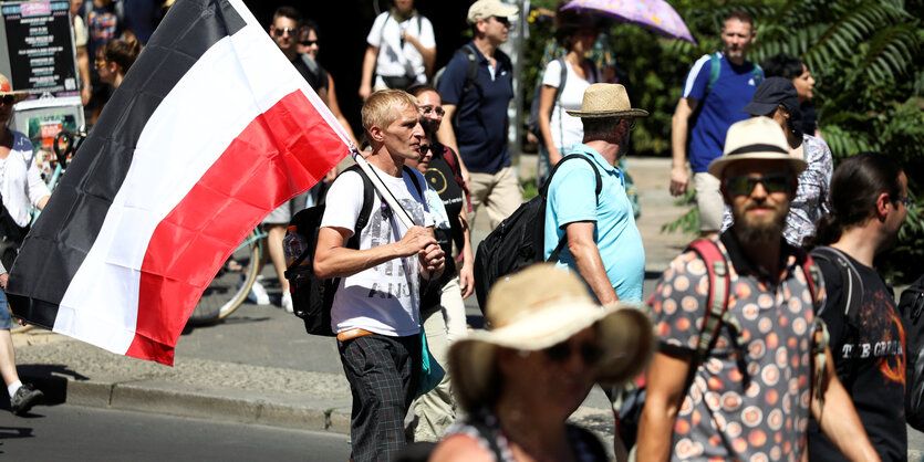 Ein Teilnehmer der Demonstration gegen die Corona-Beschränkungen trägt eine Flagge des Deutschen Reiches.