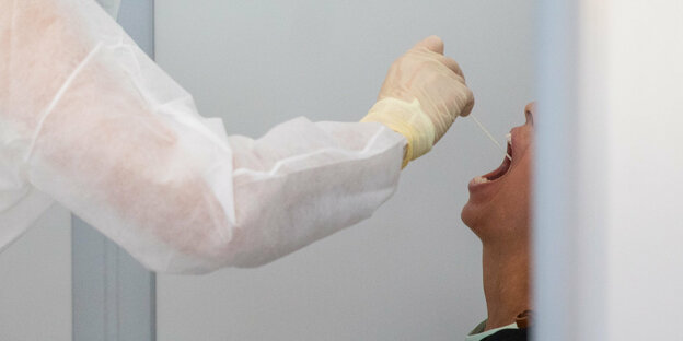 Eine Ärztin steckt einer Patientin ein Stäbchen in den Mund um einen Abstrich zu machen und auf das Coronavirus zu testen