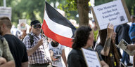 Ein Teilnehmer der Demonstration gegen die Corona-Beschränkungen trägt eine Flagge des Deutschen Reiches.