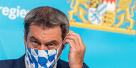 Ministerpräsident Markus Söder setzt sich eine Mund-Nasen-Maske auf.