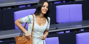 Sawsan Chebli steht lächelnd im Bundestag und fummelt an ihrer Handtasche.